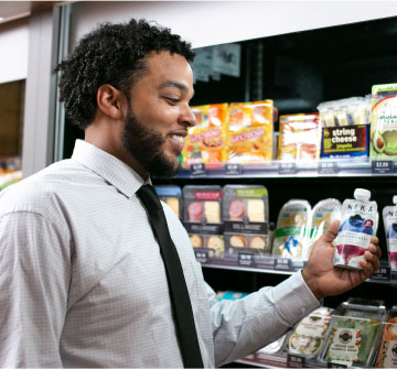 Corporate employee smiling looking at refrigerated snacks in a vending station.