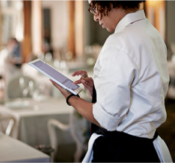 Server waiting on a table in a restaurant, entering information onto a tablet.