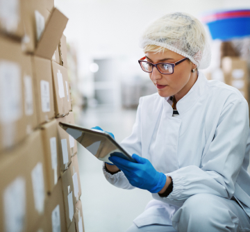 Worker with clipboard taking inventory of a stack of boxes.