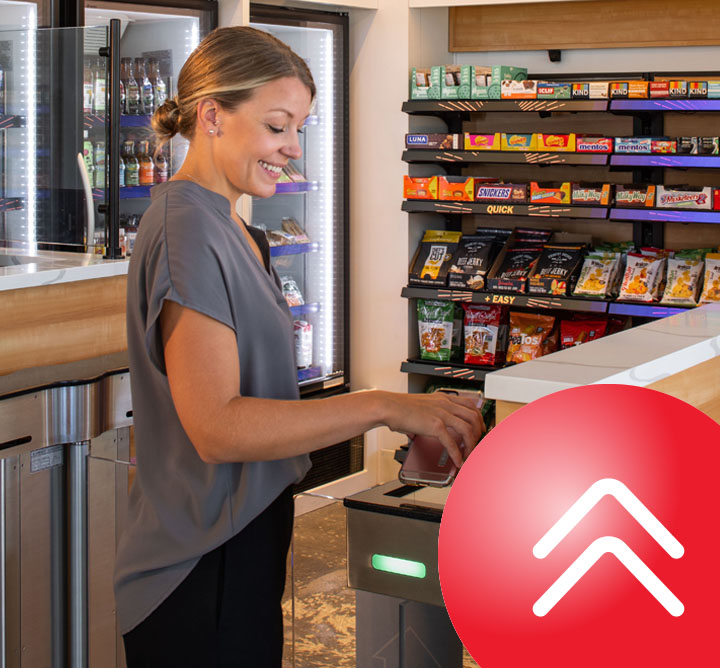A smiling woman holds her phone over the scanner at the entrance of a convenience store.