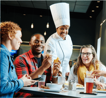 Chef smiling at a table of young people enjoying their meals.