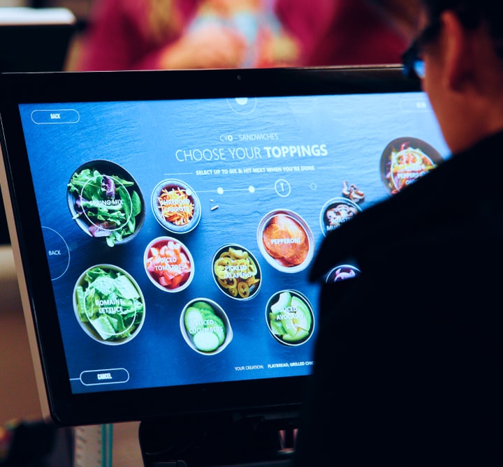 A person standing at a touchscreen food ordering device.