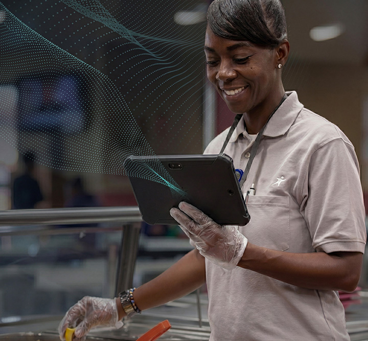 Aramark employee holds a tablet while taking the temperature at a hot food bar.