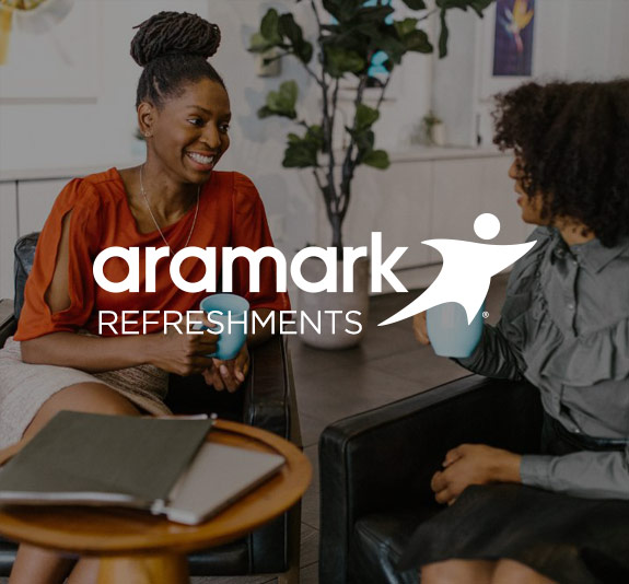 Two employees drinking coffee and talking, with the Aramark Refreshments logo.