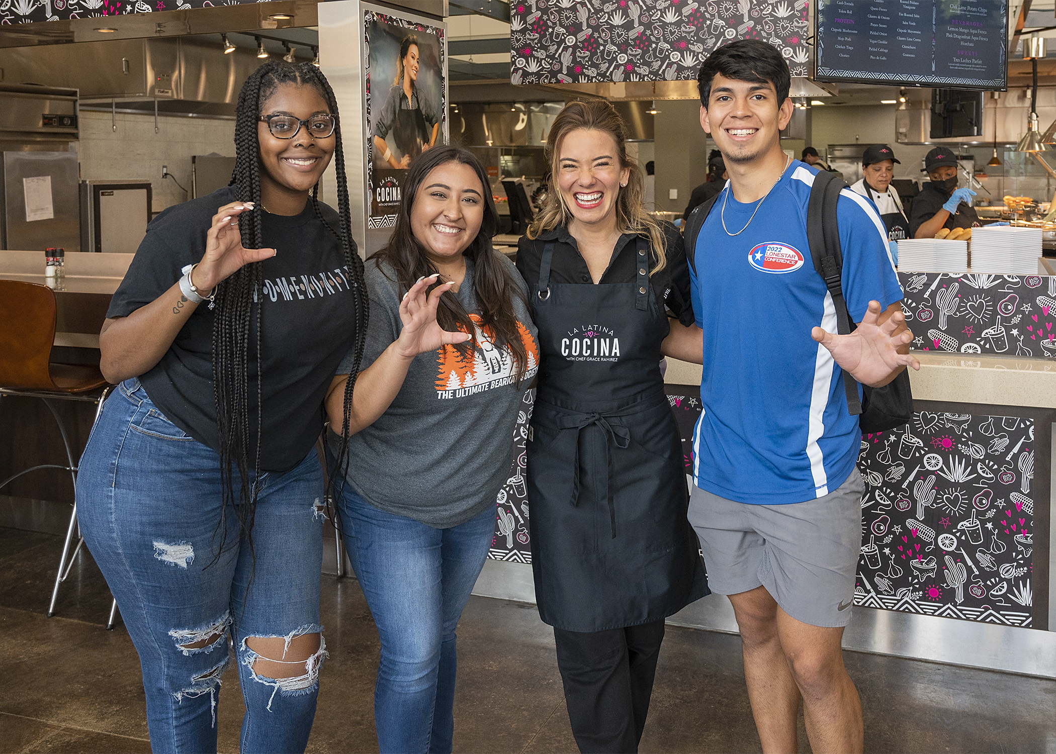 Chef Grace Ramirez wearing a La Latina Cocina apron poses with smiling college students.