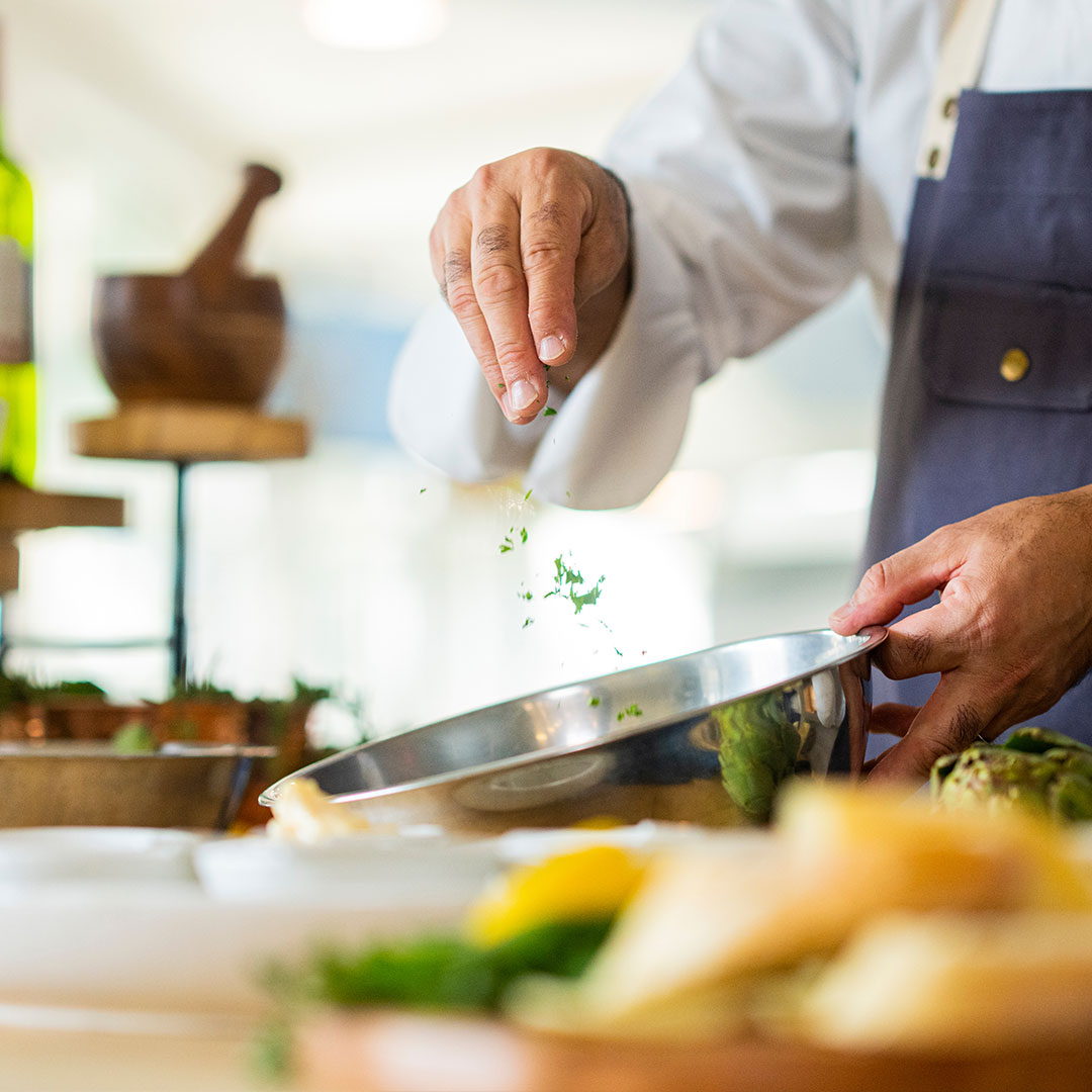 A chef sprinkling seasoning into a metal bowl.