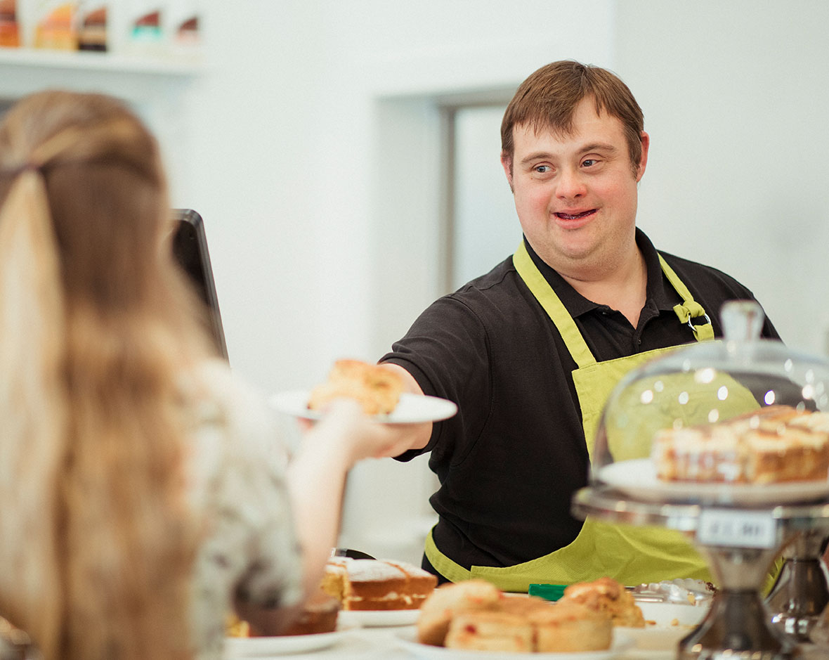 A man working a counter in a pastry shop handing a plate of food to a customer.