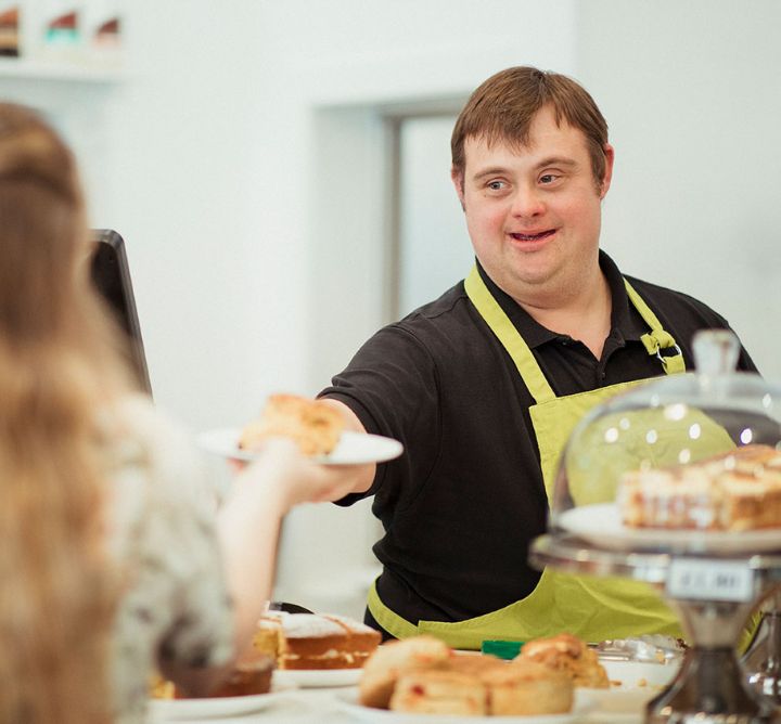 A man working a counter in a pastry shop handing a plate of food to a customer.