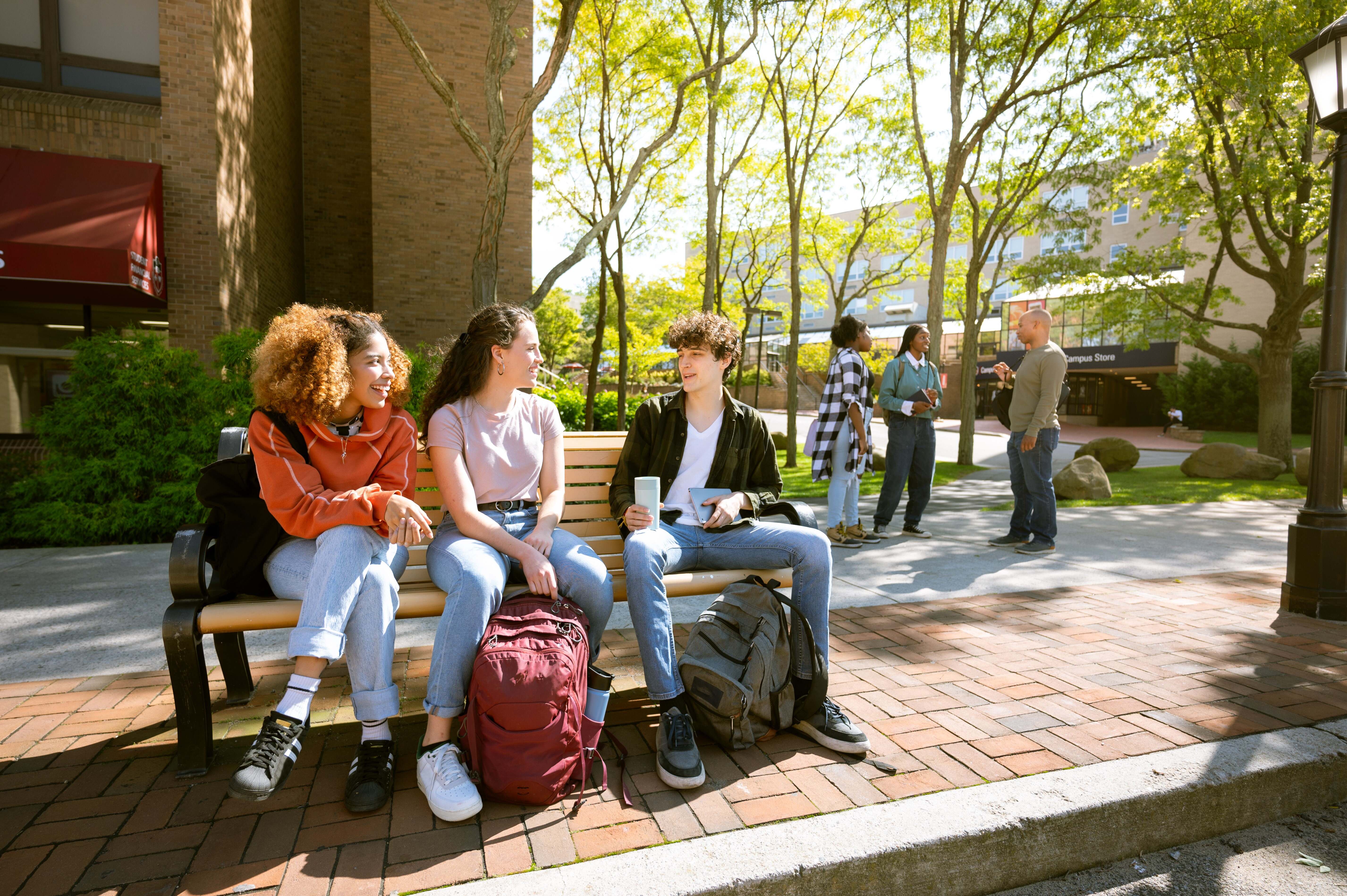 students sit on bench together on campus