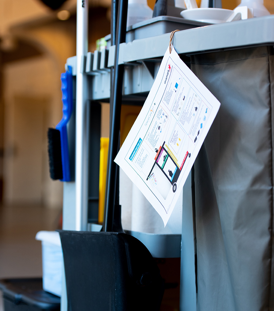 Custodial cart with an Aramark SpaceCare instruction sheet.