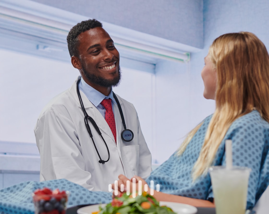 Doctor smiling at a patient in a hospital bed, with an overlaid audio symbol.