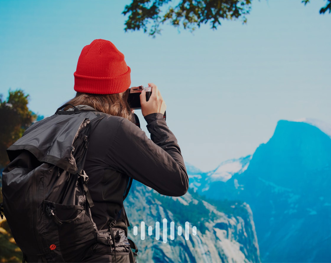Hiker taking a picture of the mountains, with an overlaid audio symbol.