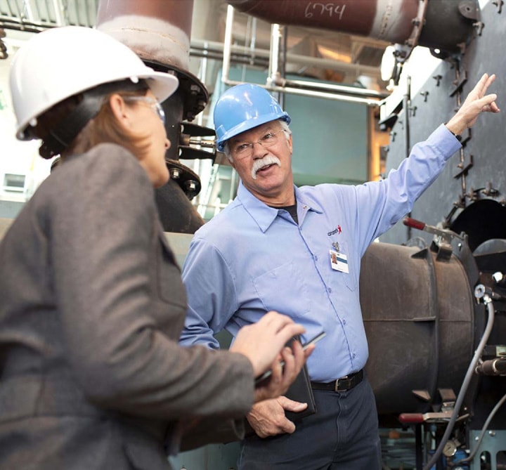 Man in hard hat pointing toward machine to woman in hard hat