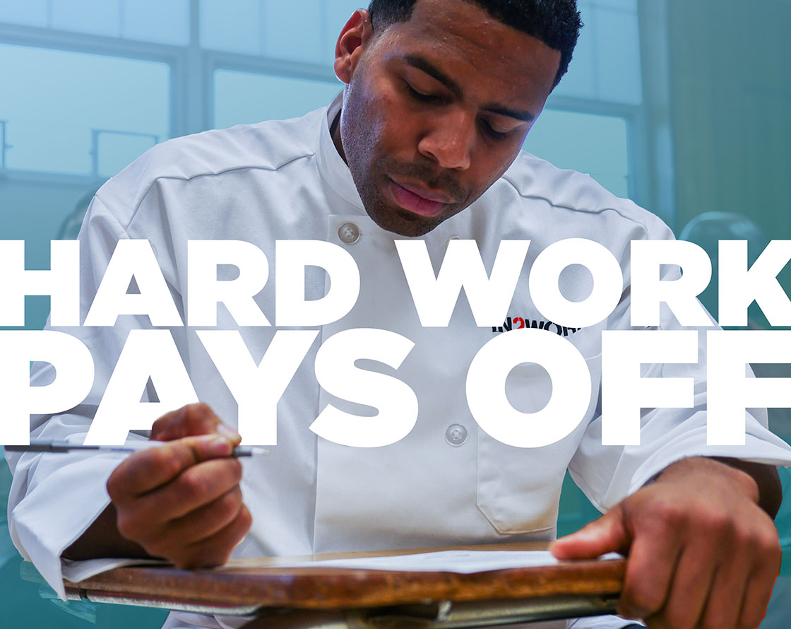 IN2WORK fellow wearing a chef's jacket writing at a desk, overlaid by the words hard work pays off.