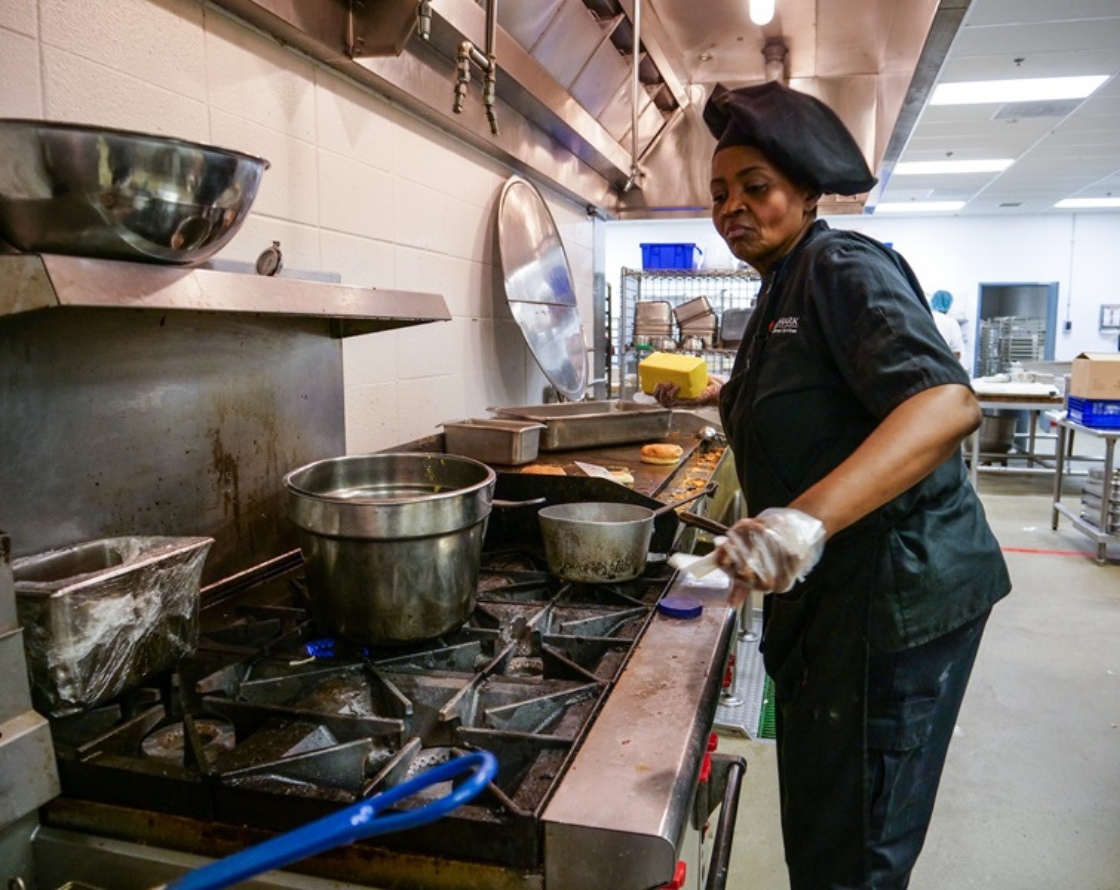 IN2WORK fellow in a black cook's uniform standing at an industrial stove.