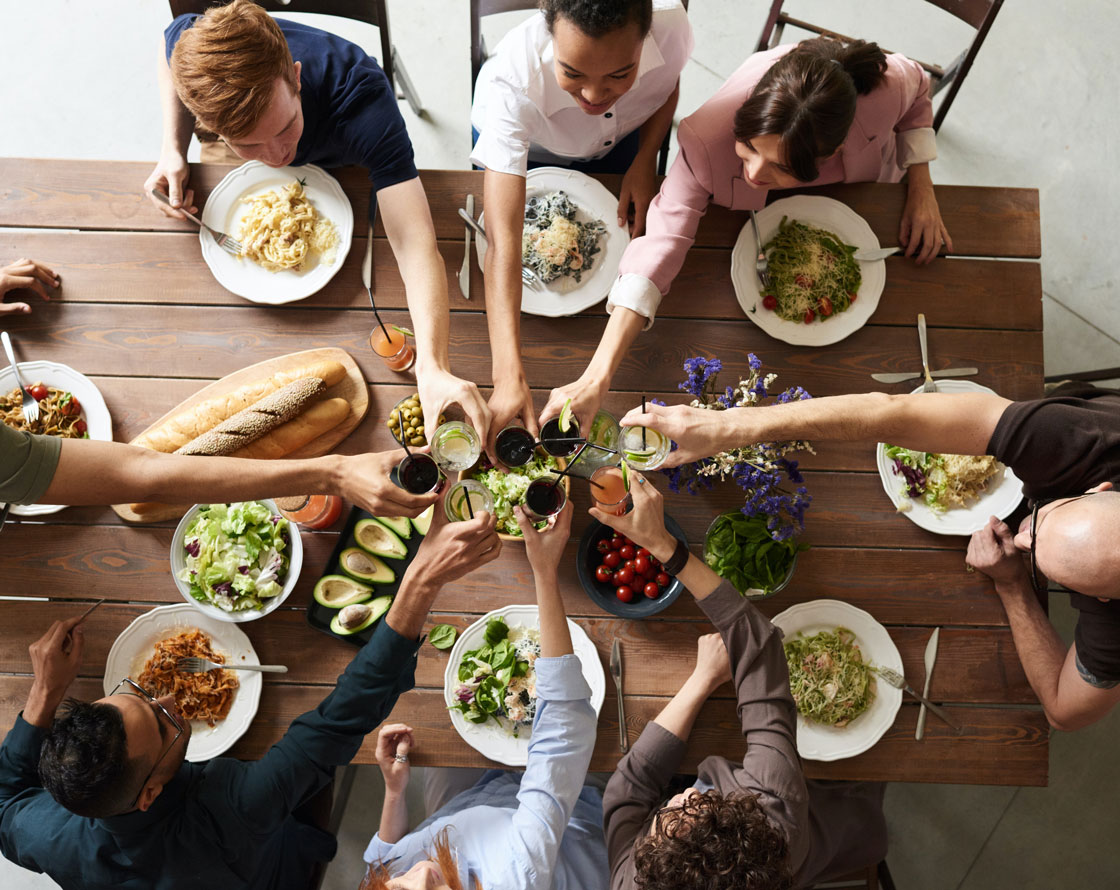 Friends toasting their drinks over a table of food.
