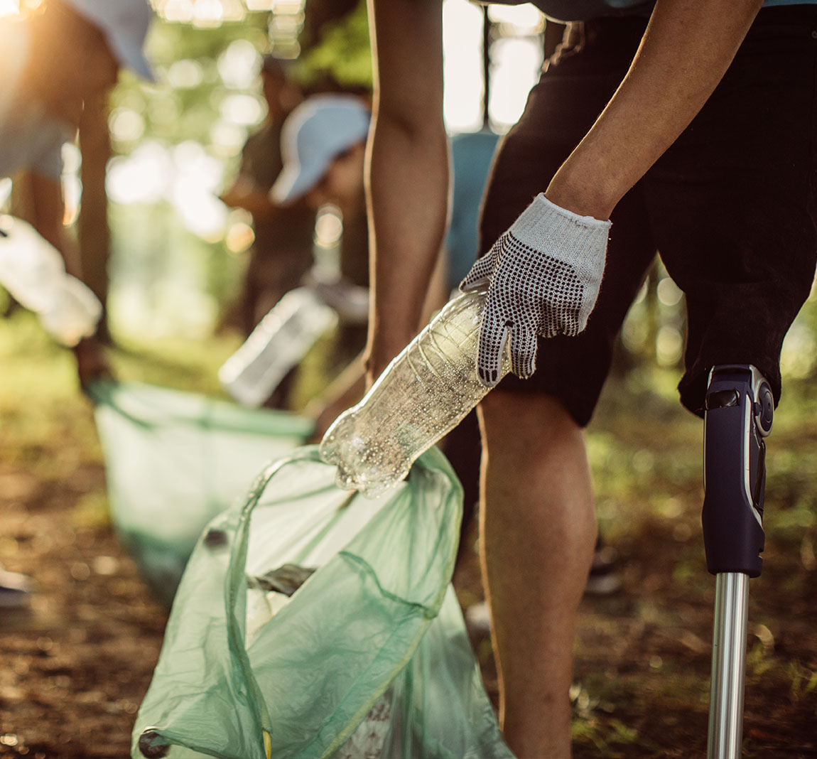 A person with a prosthetic leg picks up a recycled bottle and puts it into a plastic bag.