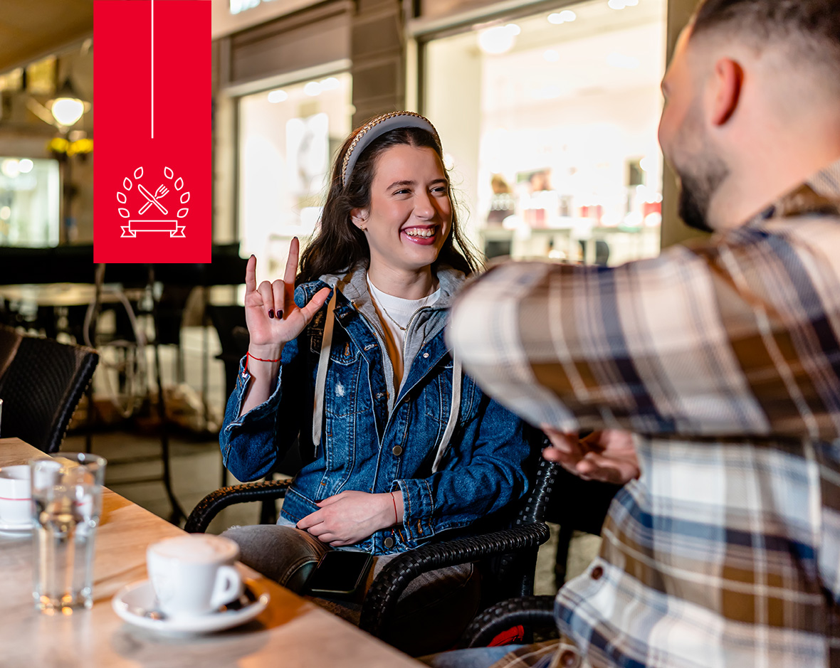 A woman using sign language with her friend in a dining hall.