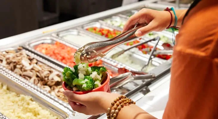 A student taking food from a salad bar.