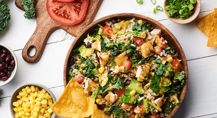 A large salad in a wooden bowl surrounded by fresh ingredients in smaller bowls.