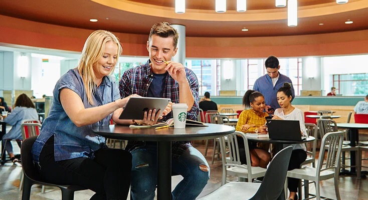 Students sitting together at a cafe table, looking at a tablet.