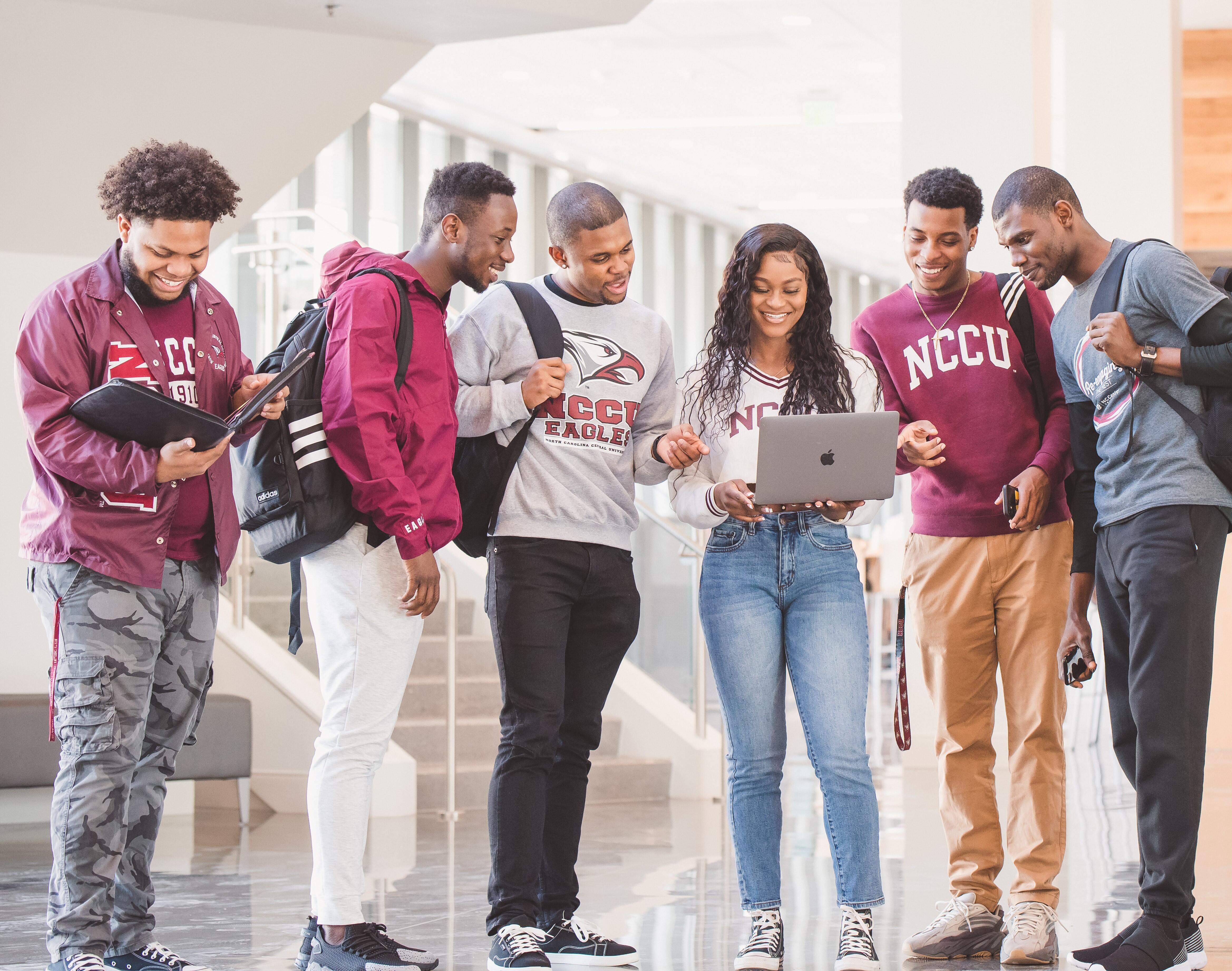6 NCCU students pose together in dining hall, look at laptop