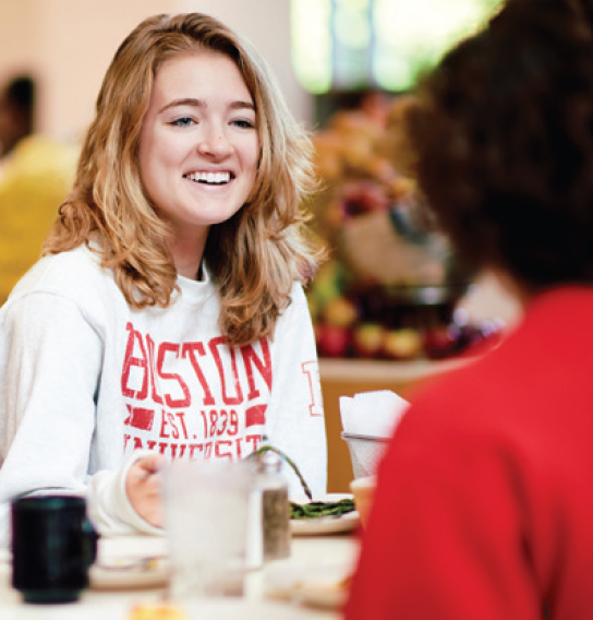student wearing Boston University sweatshirt sitting at table