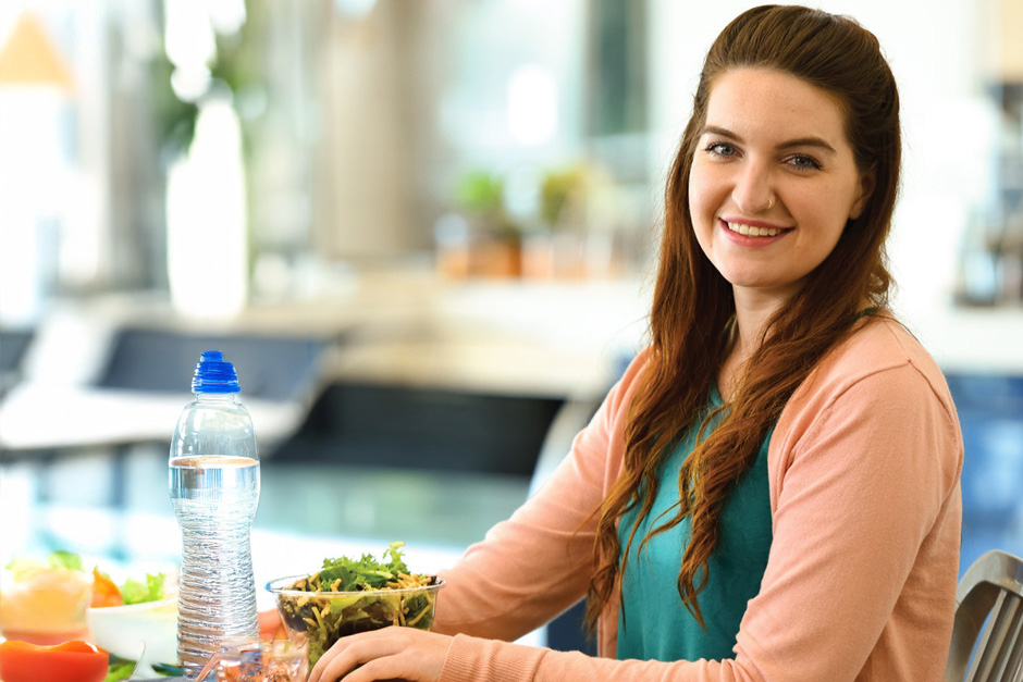 A smiling college student eating a salad in the dining hall.