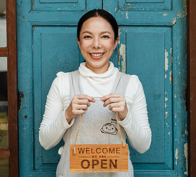 A young Asian woman smiling and holding up a wooden welcome sign.