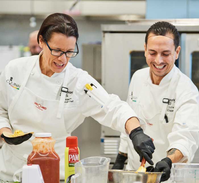 Two Aramark chefs smiling and laughing together while preparing food.
