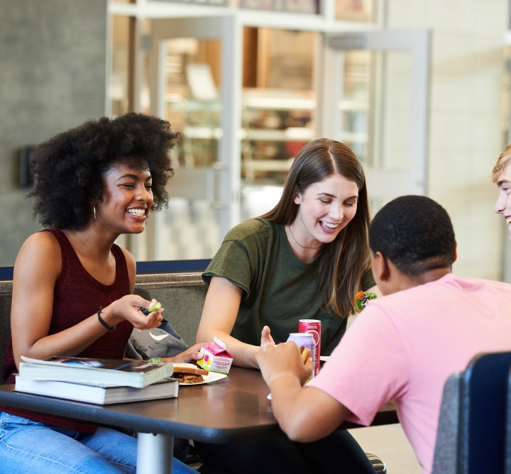 Teenagers eating and laughing in a cafeteria.
