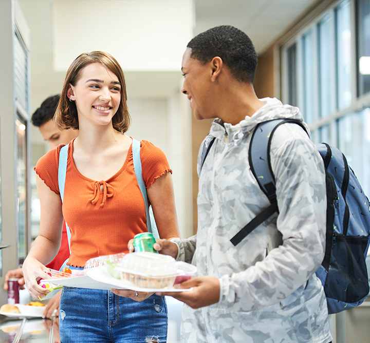 Kids talking and smiling while getting food at a school cafe.