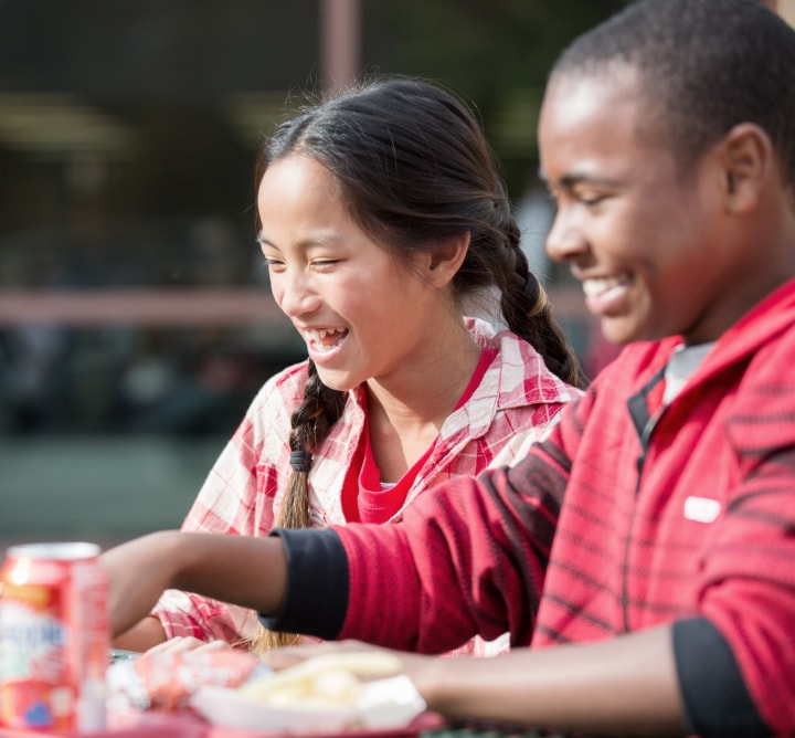 Two kids laughing and eating lunch.