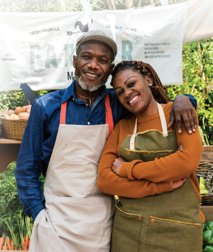 man and woman wearing aprons in front of farm stand