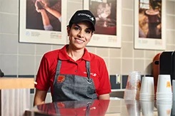 Smiling Aramark worker in an apron standing behind a counter.