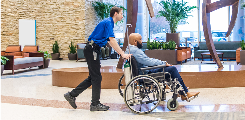 A hospital employee pushing a man in a wheelchair.