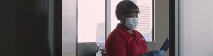 An Aramark employee wearing PPE using her phone in an office.