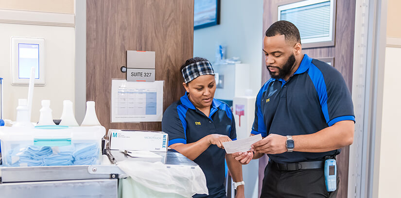 Hospital environmental services workers talking next to a cleaning cart.