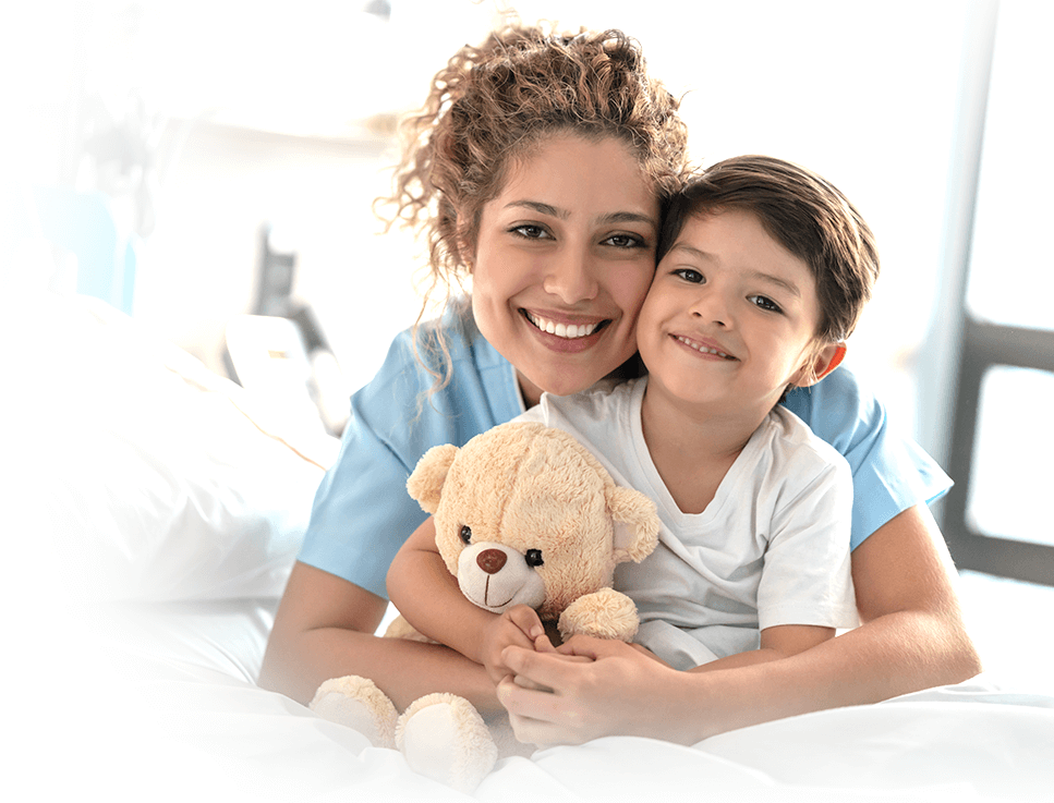 A nurse hugging a young patient holding a teddy bear.
