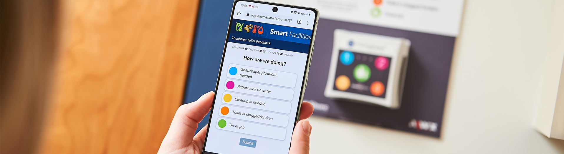 A hand holding a mobile phone with the Smart Facilities feedback interface.
