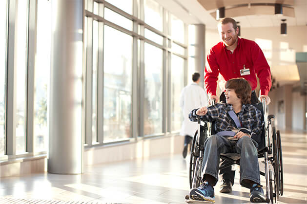 Healthcare worker pushing a young patient in a wheelchair.