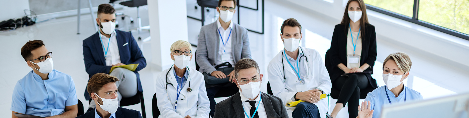 Healthcare professionals in masks sitting in chairs watching a presentation.