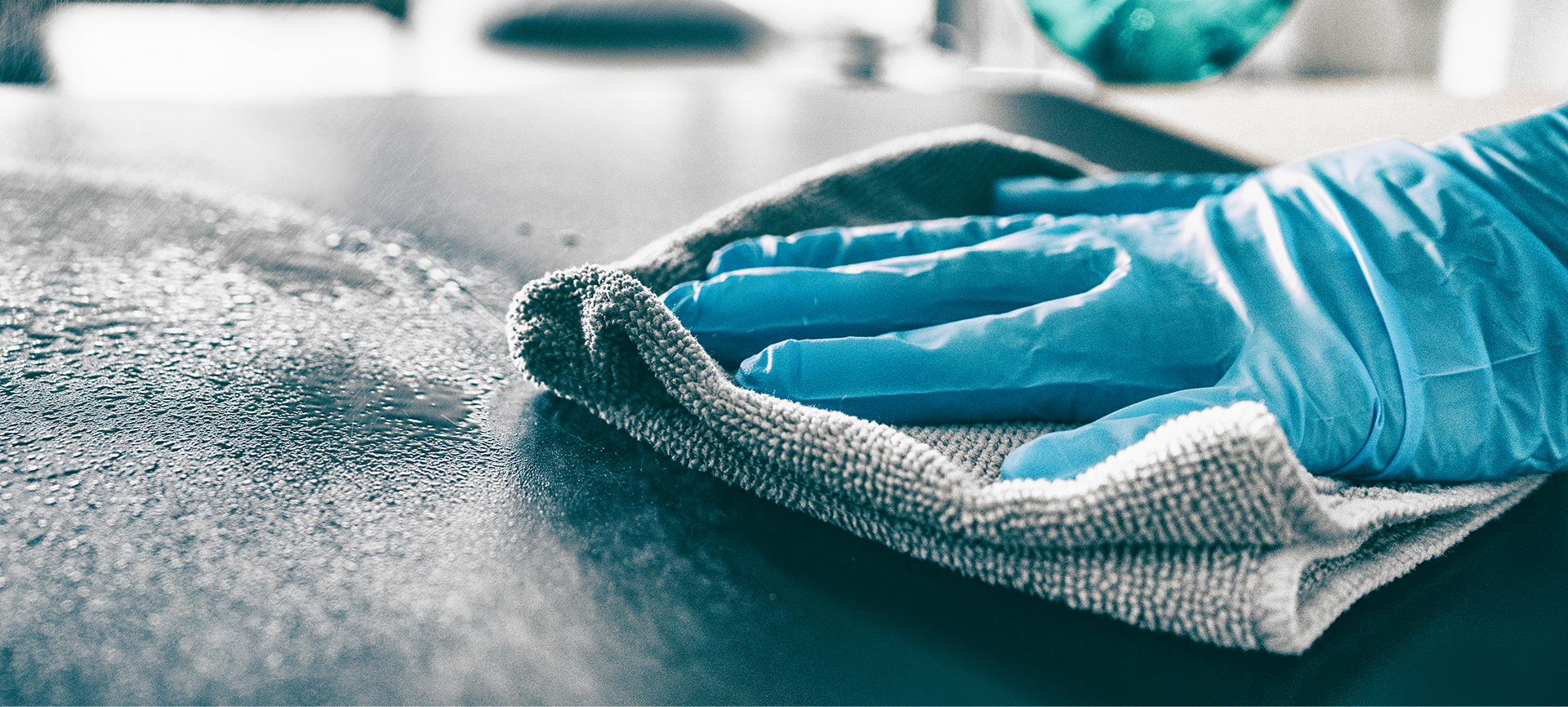 A gloved hand using a cloth to wipe down a surface.