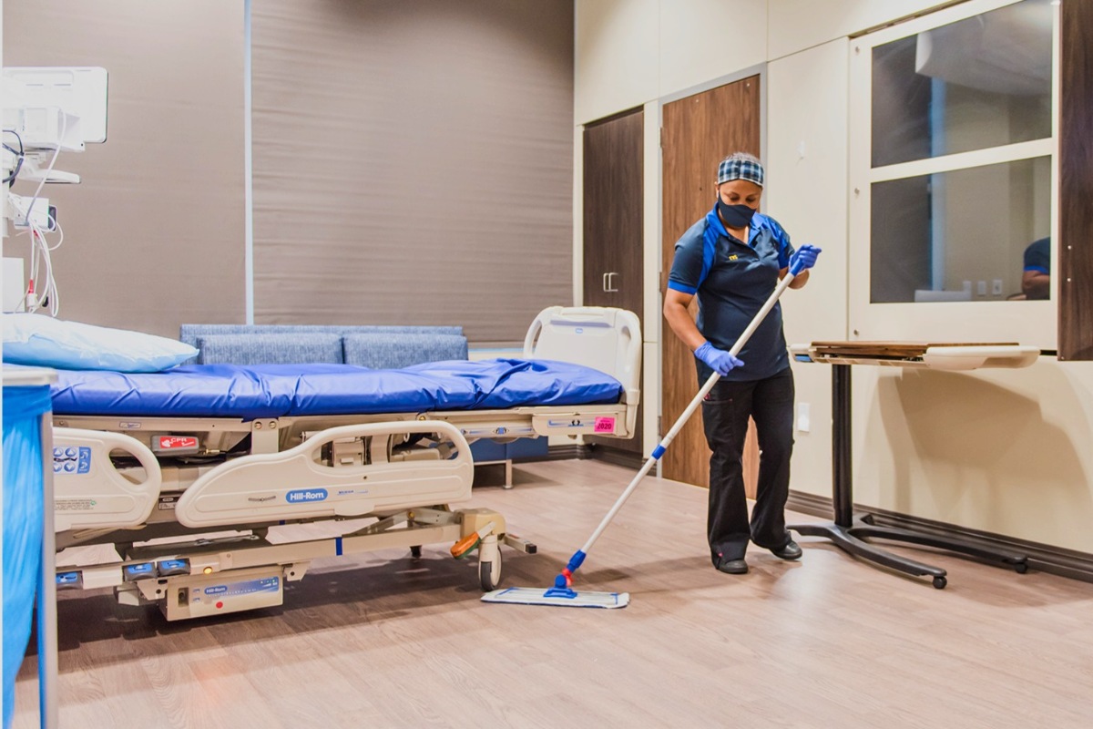 A healthcare worker wearing PPE mopping the floor of a hospital room.