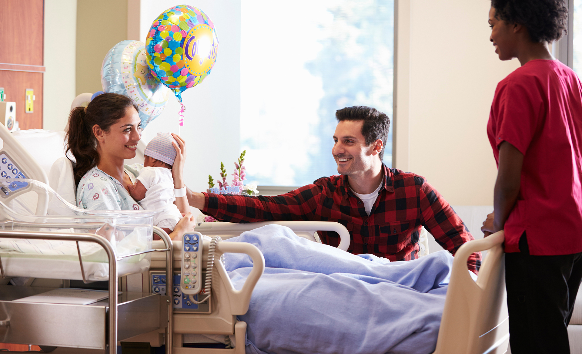 A mother and newborn baby resting in a hospital bed surrounded by well-wishers.