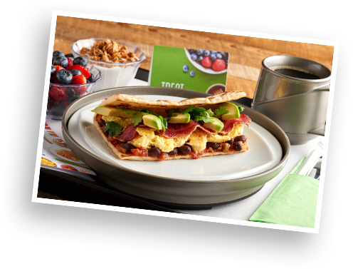 A breakfast wrap, fresh fruit, yogurt, and coffee on a tray.