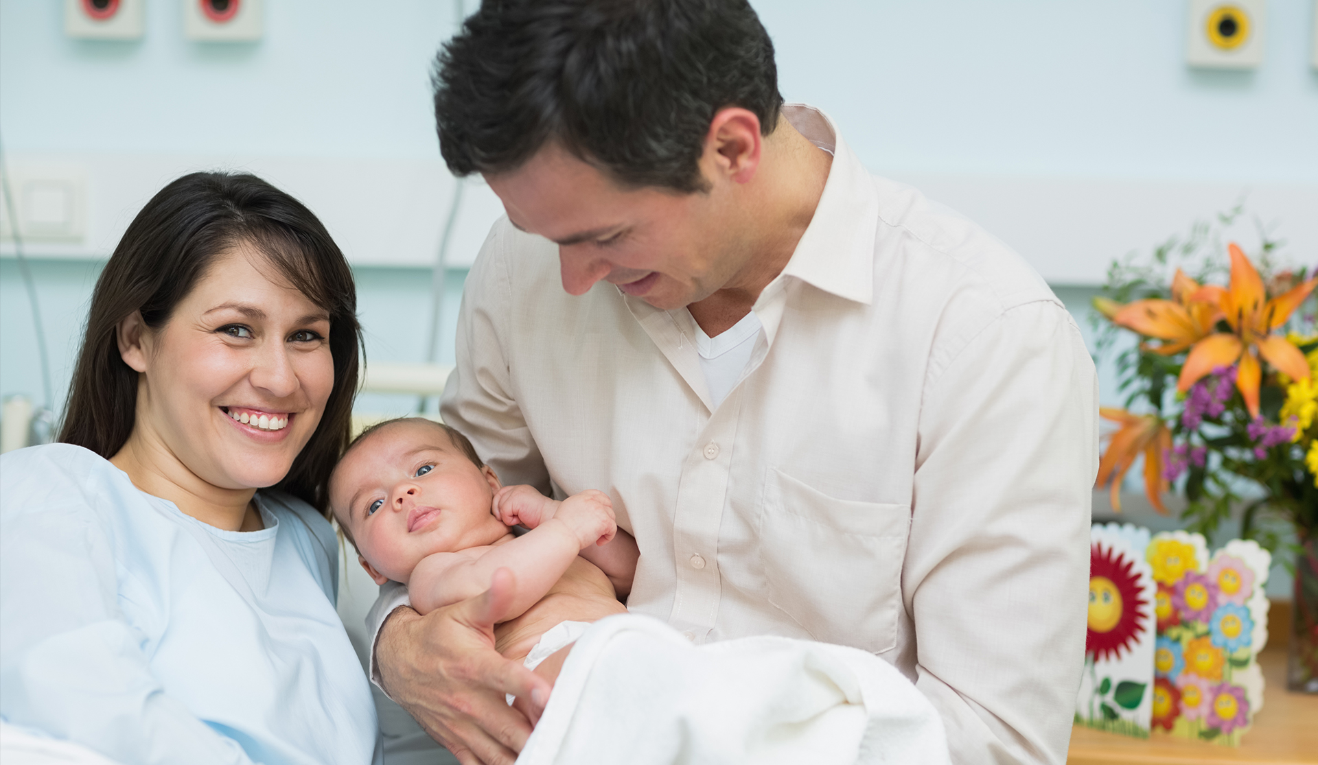 A smiling young mother and father holding a newborn baby.