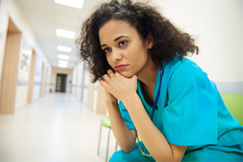 Tired nurse resting her head in her hands while sitting in a hospital hallway.