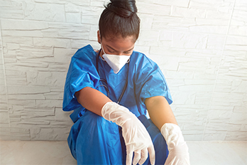 Exhausted nurse wearing personal protective equipment resting against a wall.