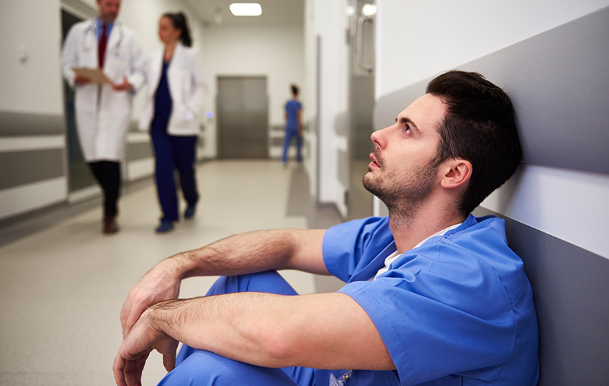 Tired nurse sitting on the floor of a hospital hallway.